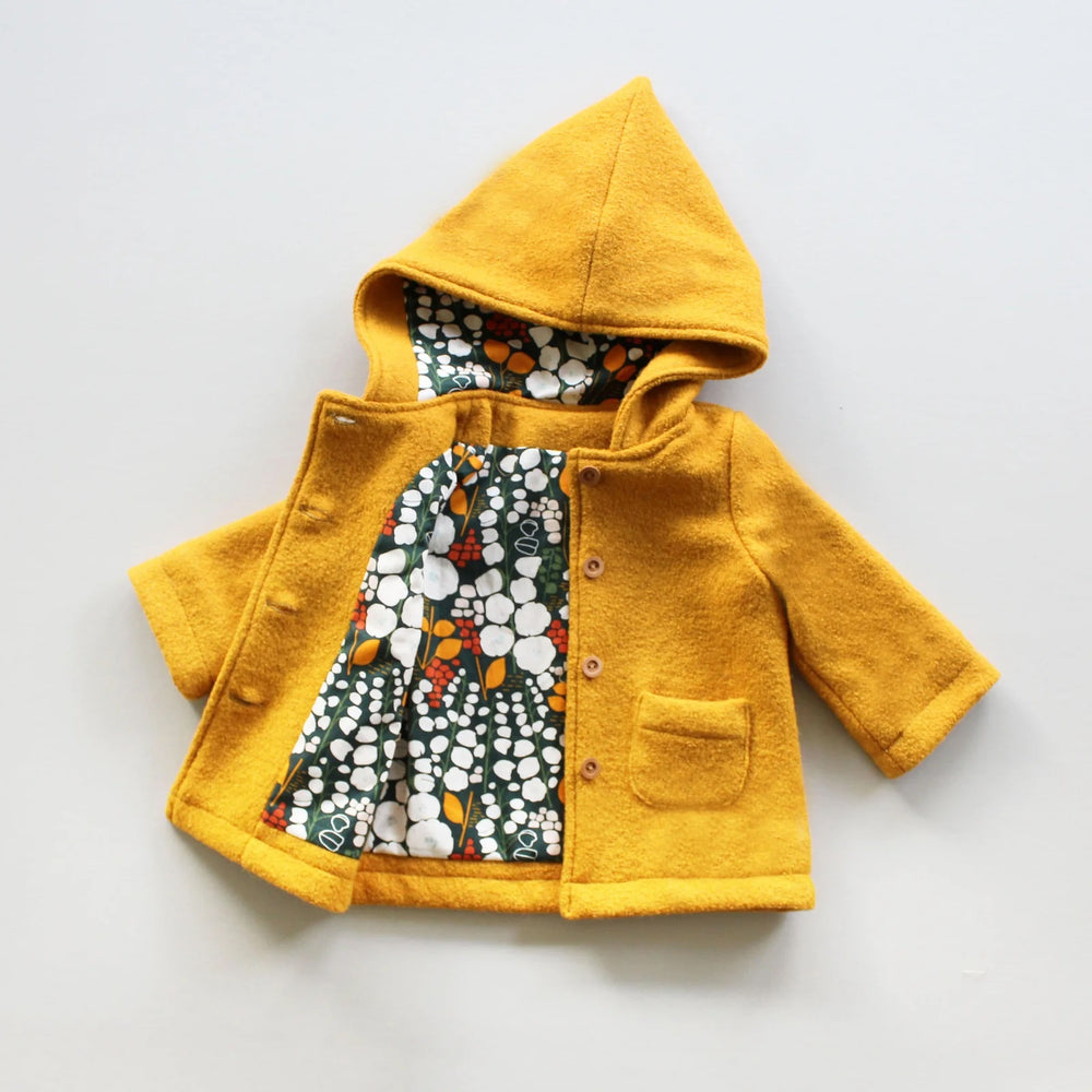The Baby/Child Cardamon Coat sewing pattern from Oh Me Oh My Sewing on The Fold Line. A coat pattern made in wool coating, fleece, or canvas fabric, featuring a full lining, pixie hood, patch pockets, and button closure.