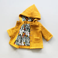 The Baby/Child Cardamon Coat sewing pattern from Oh Me Oh My Sewing on The Fold Line. A coat pattern made in wool coating, fleece, or canvas fabric, featuring a full lining, pixie hood, patch pockets, and button closure.