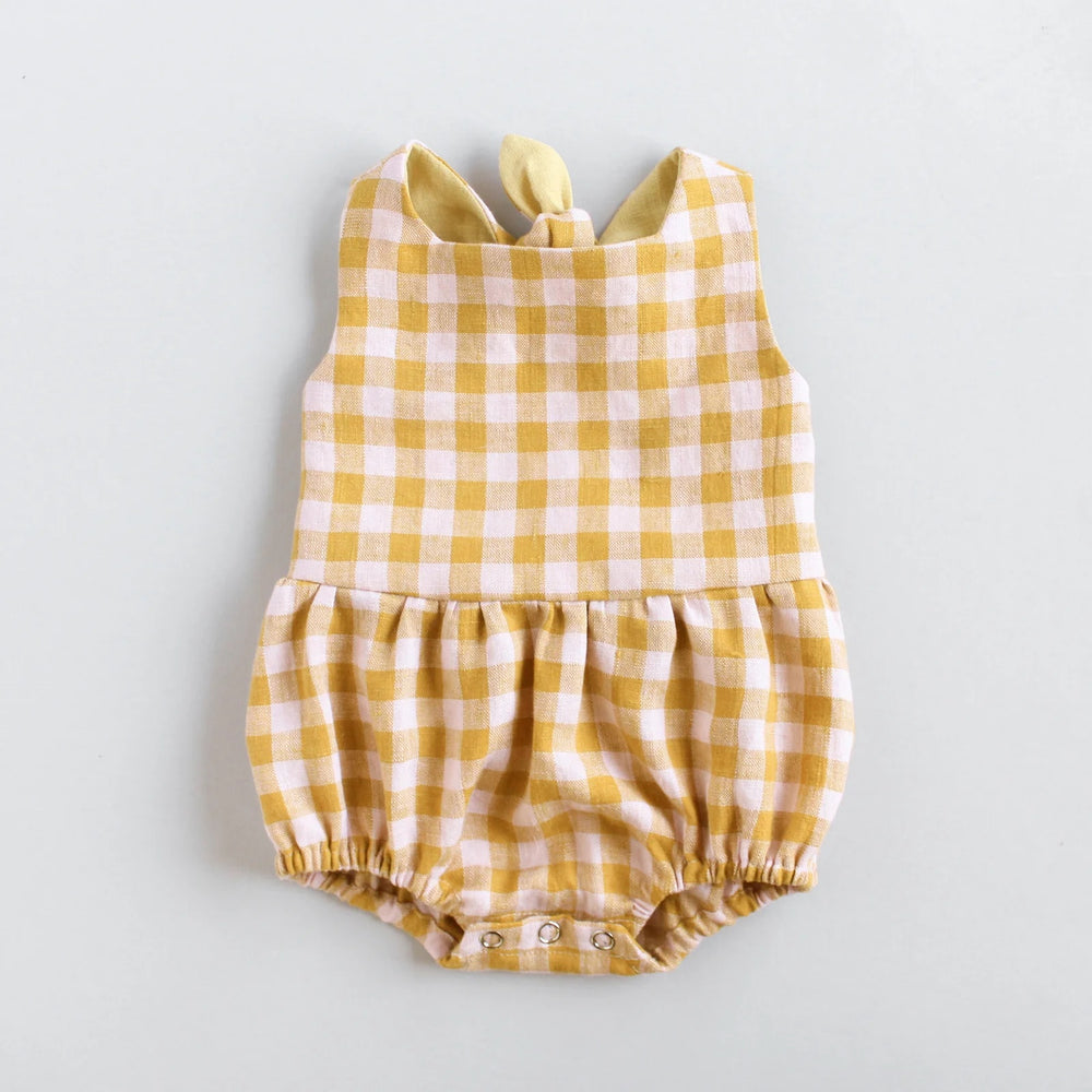 The Baby/Child Dandelion Romper sewing pattern from Oh Me Oh My Sewing on The Fold Line. A romper pattern made in quilting cotton, washed linen, double gauze, cotton lawn, voile, or rayon challis fabric, featuring a square neckline, lined bodice, tie back with elastic, and gathered bottom with a snap opening. 
