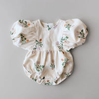 The Baby/Child Larkspur Romper sewing pattern from Oh Me Oh My Sewing on The Fold Line. A romper pattern made in quilting cotton, washed linen, double gauze, cotton lawn, voile, or rayon challis fabric, featuring a bubble silhouette, round neckline, puff sleeves, and gathered bottom with snap opening.