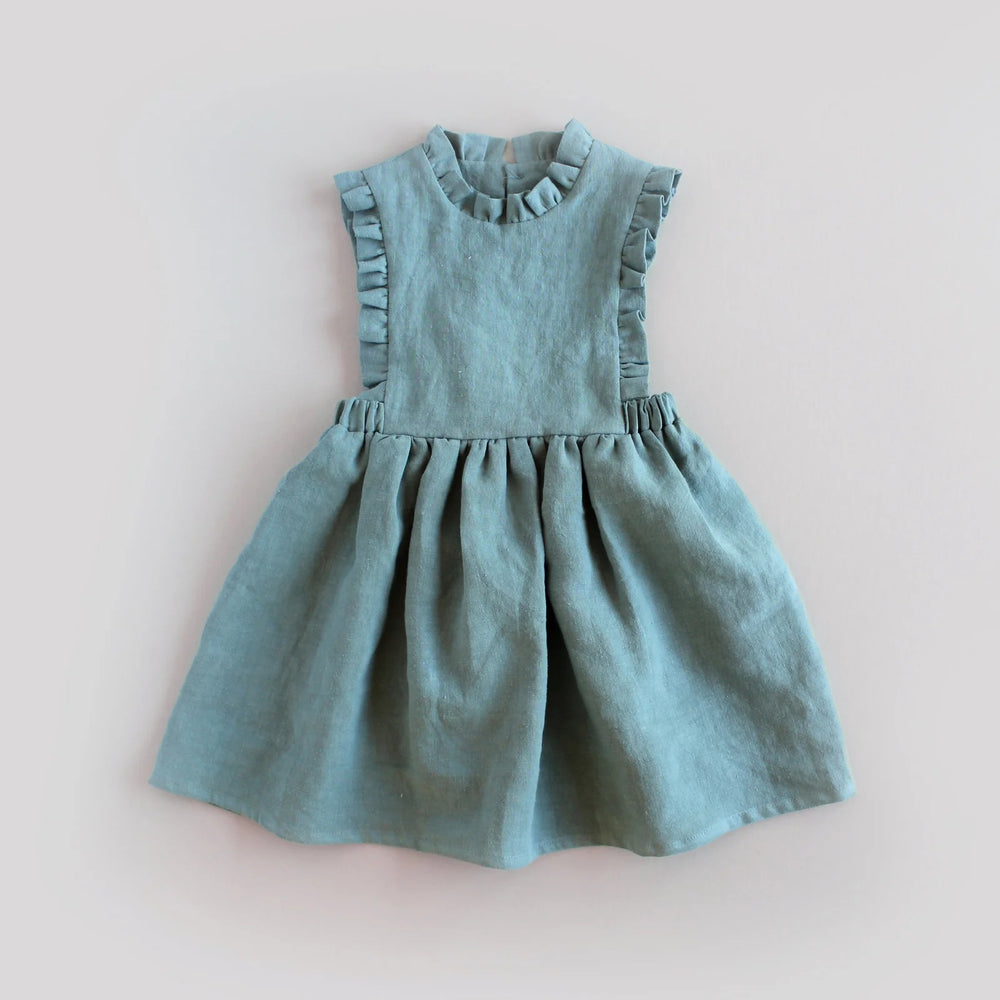The Baby/Child Lily of the Valley Pinafore sewing pattern from Oh Me Oh My Sewing on The Fold Line. A pinafore dress pattern made in quilting cotton, washed linen, double gauze, cotton lawn, voile, or rayon challis fabric, featuring a bib bodice with ruffles, full gathered skirt, elastic at the sides, and keyhole closure at the back.