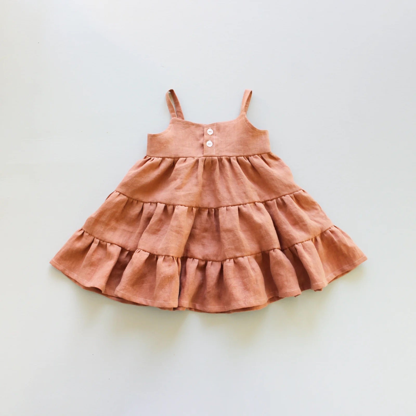 The Baby/Child Magnolia Dress sewing pattern from Oh Me Oh My Sewing on The Fold Line. A dress pattern made in quilting cotton, washed linen, double gauze, cotton lawn, voile, or rayon challis fabric, featuring a button up bodice, thin straps, and tiered skirt.
