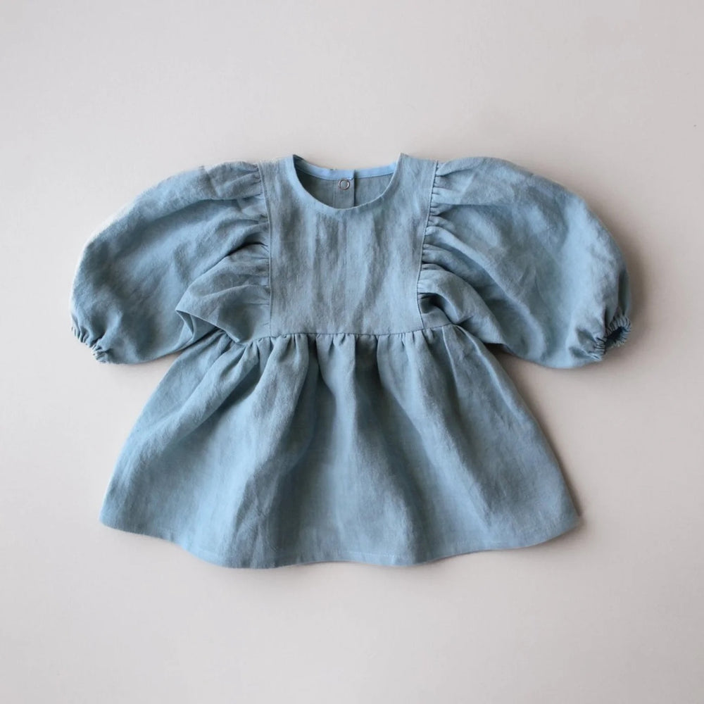 The Baby/Child Maisie Dress sewing pattern from Oh Me Oh My Sewing on The Fold Line. A dress pattern made in quilting cotton, washed linen, double gauze, cotton lawn, voile, or rayon challis fabric, featuring a round neckline, puff sleeves, and gathered skirt.
