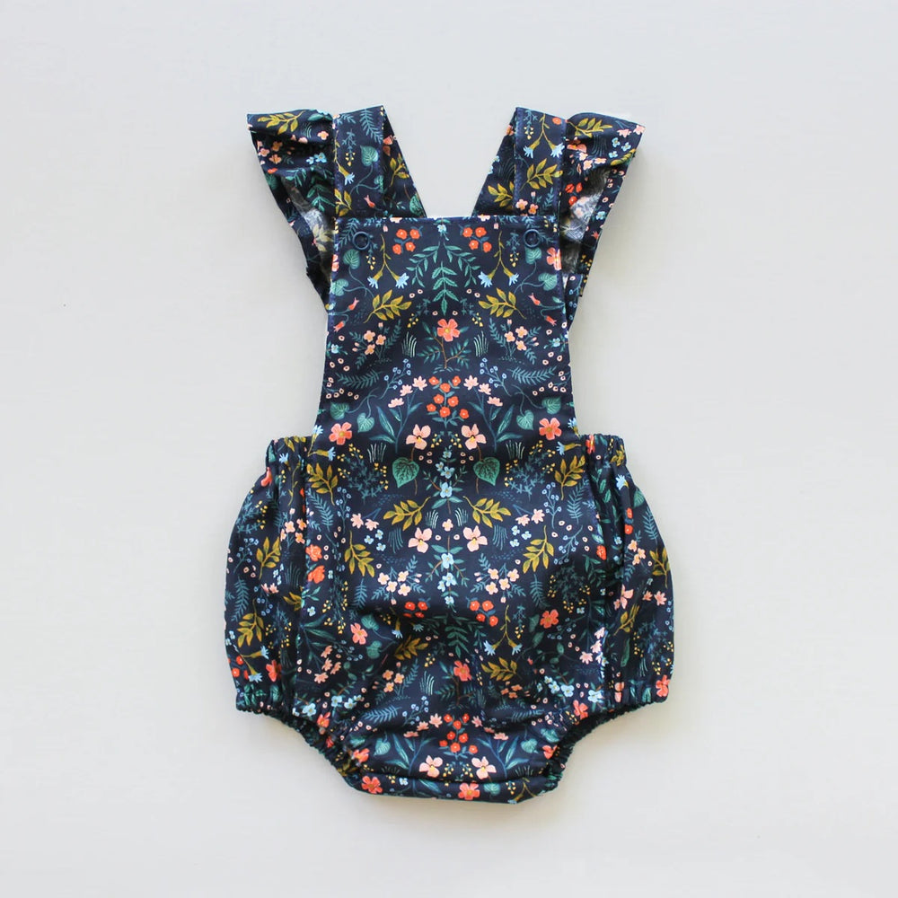 The Baby/Child Overall Playsuit sewing pattern from Oh Me Oh My Sewing on The Fold Line. A playsuit pattern made in quilting cotton, lighter canvases, twill, corduroy, or washed linen fabric, featuring a bib, crossed adjustable straps with ruffles, elastic in the back, and elastic legholes.