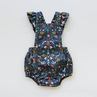 The Baby/Child Overall Playsuit sewing pattern from Oh Me Oh My Sewing on The Fold Line. A playsuit pattern made in quilting cotton, lighter canvases, twill, corduroy, or washed linen fabric, featuring a bib, crossed adjustable straps with ruffles, elastic in the back, and elastic legholes.