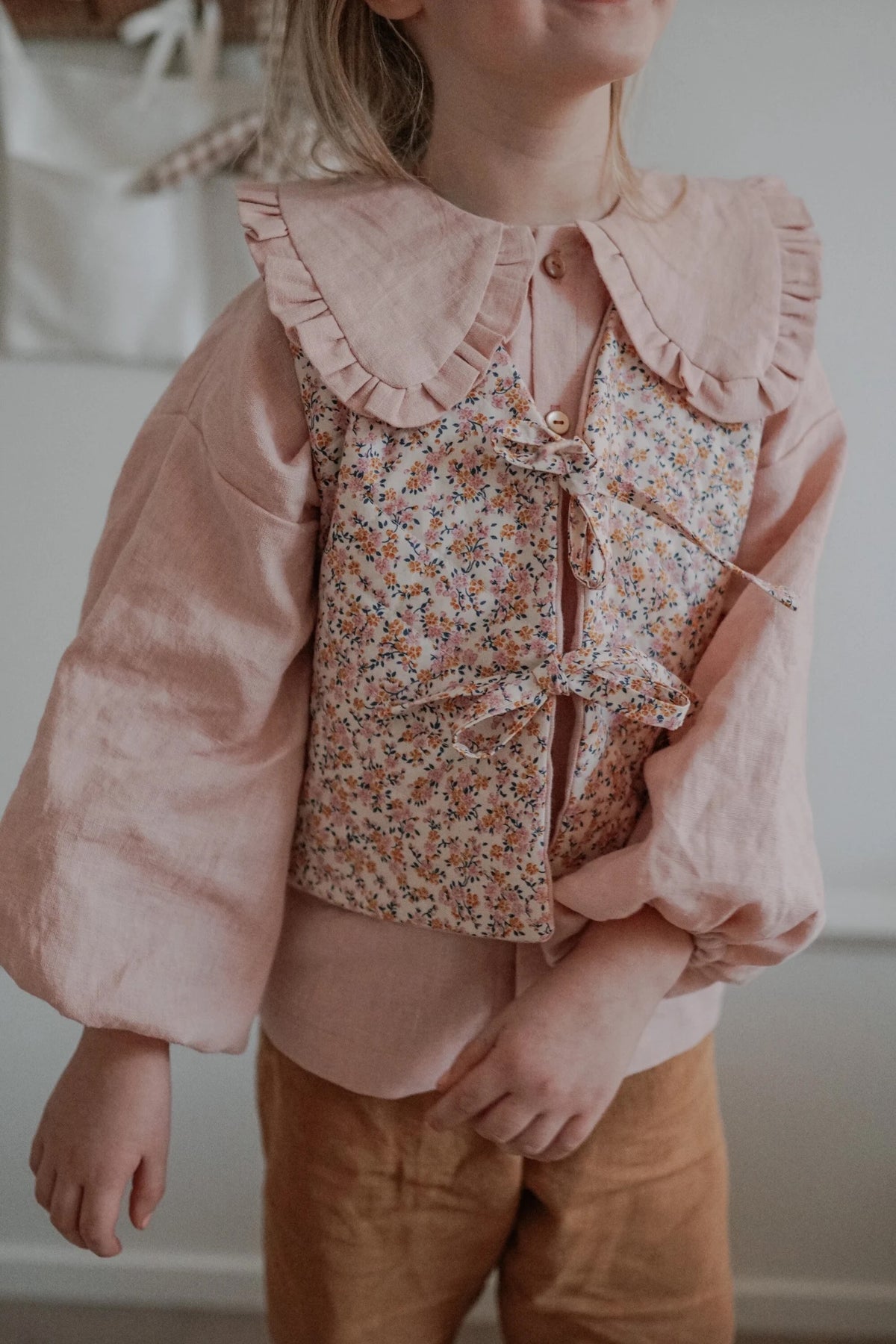 Girl wearing the Baby/Child Pippa Vest sewing pattern from Me & Kiddo Patterns on The Fold Line. A reversible quilted vest pattern made in linen or cotton fabric, featuring a straight cut, V-neckline, and two ties at the front.