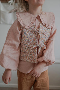Girl wearing the Baby/Child Pippa Vest sewing pattern from Me & Kiddo Patterns on The Fold Line. A reversible quilted vest pattern made in linen or cotton fabric, featuring a straight cut, V-neckline, and two ties at the front.