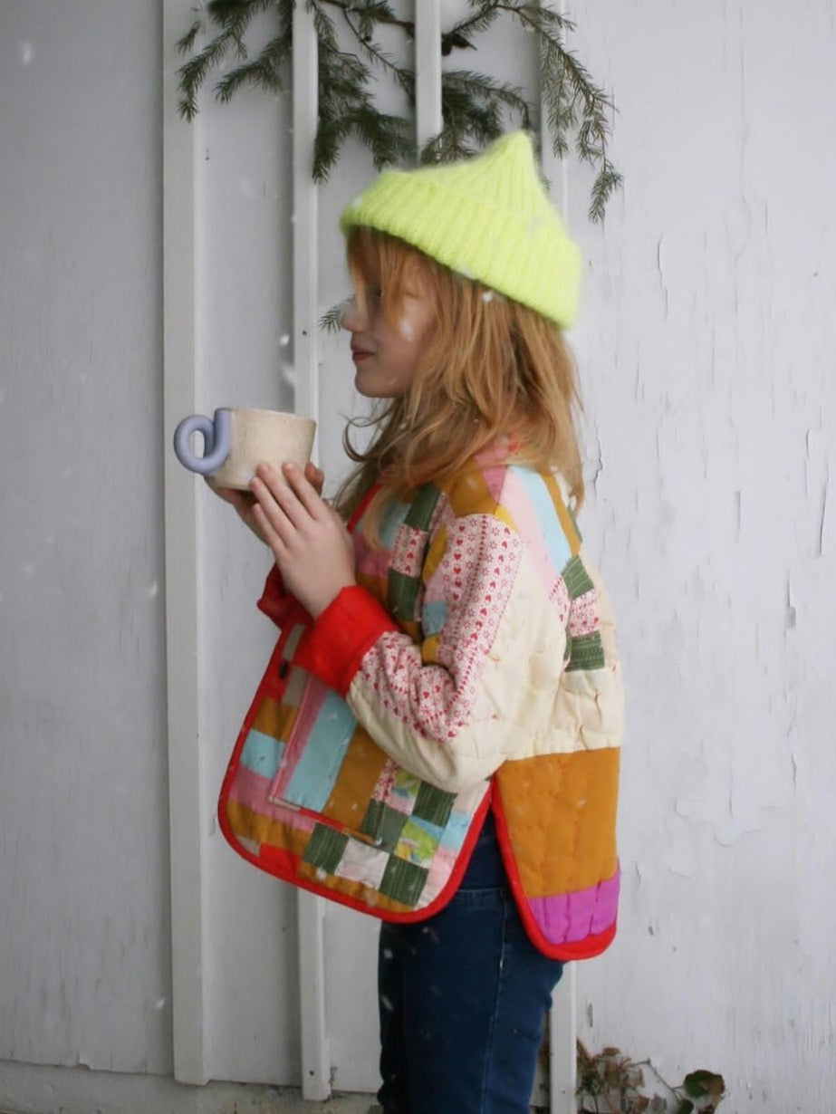 Girl wearing the Baby/Child Rue Quilt Coat sewing pattern from Spaghetti Western Sewing on The Fold Line. A quilted jacket pattern made in quilting cotton, linen, pre-quilted fabric, or upcycled blankets, featuring a relaxed oversized fit, collar, side splits, and patch pockets.