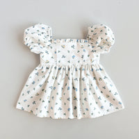 The Baby/Child Sophie Dress sewing pattern from Oh Me Oh My Sewing on The Fold Line. A dress pattern made in quilting cotton, washed linen, cotton lawn, voile, or rayon challis fabric, featuring a square neckline with a ruffle, empire waist, short puff sleeves, gathered skirt, and button closure at the back.