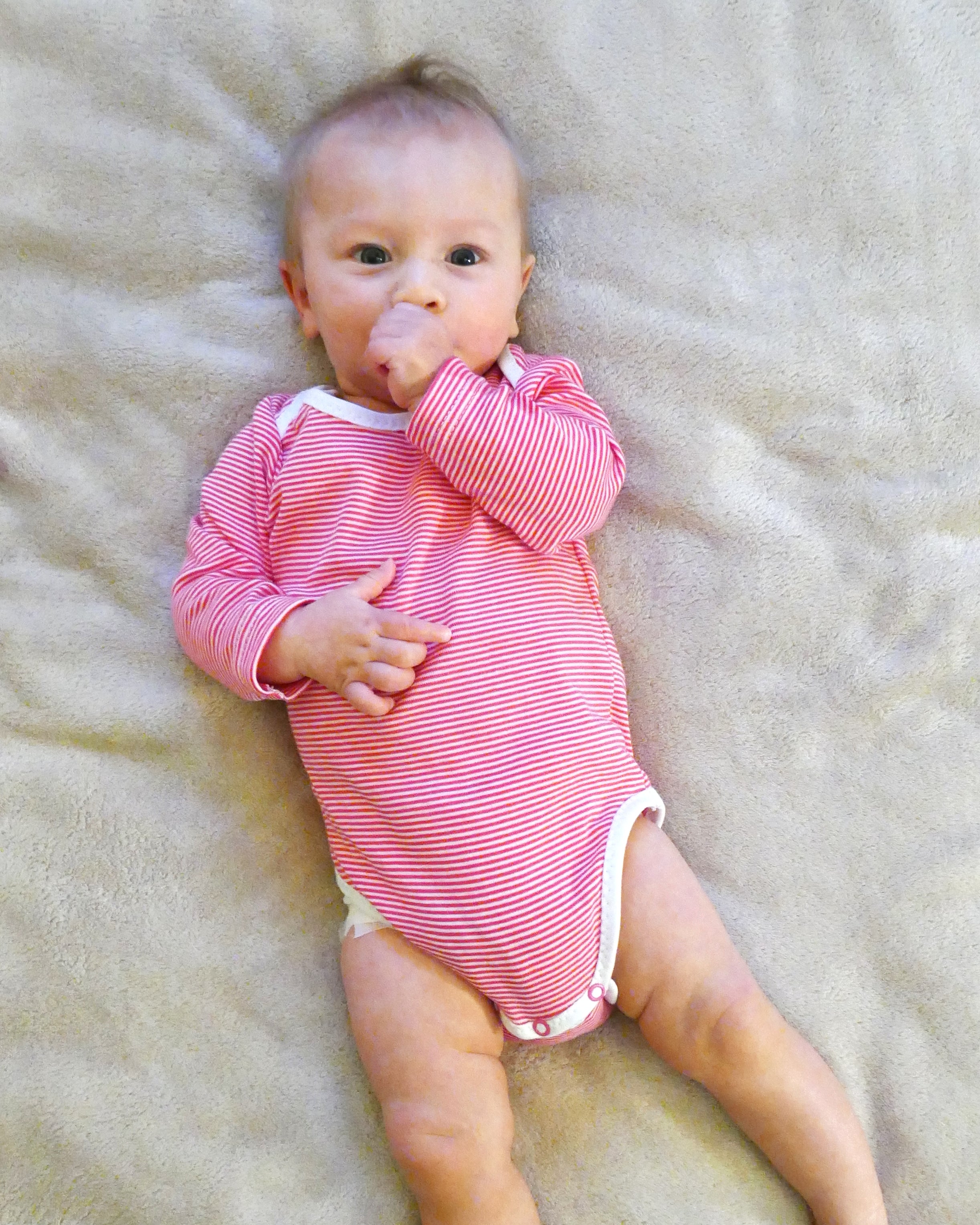 Baby wearing the Baby/Child Youpi Bodysuit sewing pattern from Petits D'om on The Fold Line. A bodysuit pattern made in knit fabric, featuring an envelope neck, long sleeves, and snap crotch.