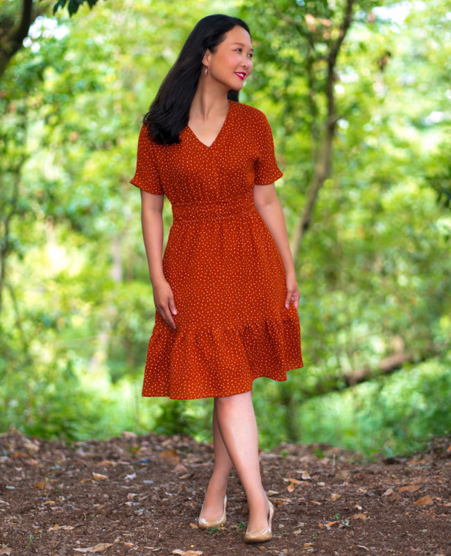 Woman wearing the Baiona Dress sewing pattern from Itch to Stitch on The Fold Line. A dress pattern made in chambray, rayon challis, batiste, double gauze, shirting, lightweight linen, or lightweight broadcloth fabric, featuring a V-neck, grown-on short sleeves, elastic waist, A-line skirt, pockets, ruffled hem, and knee length.