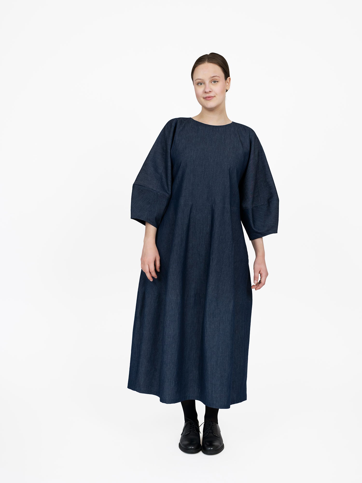 Woman wearing the Barrel Dress sewing pattern from The Assembly Line on The Fold Line. A dress pattern made in light to medium weight fabric, featuring a round neckline, long sculpted batwing sleeves, and a midi length skirt.