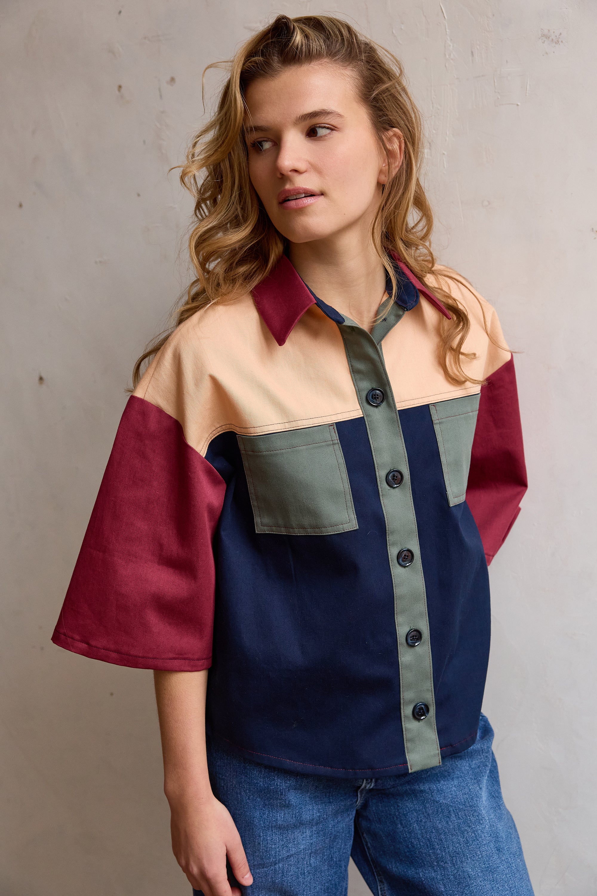 Woman wearing the Bertie Shirt sewing pattern from Atelier Jupe on The Fold Line. A shirt pattern made in cotton, linen, viscose, or tencel fabric, featuring a relaxed fit, collar with a stand, yoke, button front, pockets, elbow length sleeves, and rounded hem.