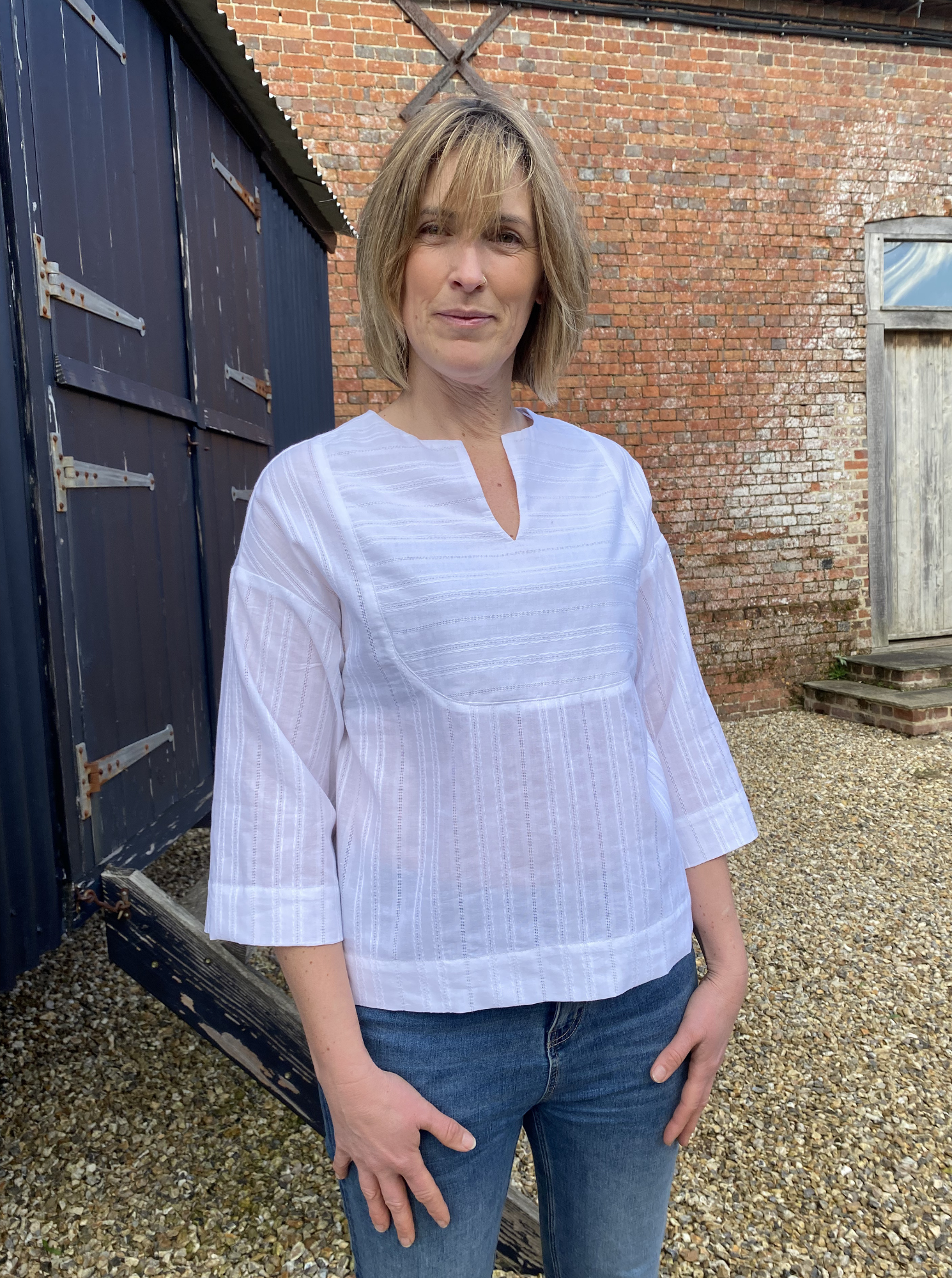 Woman wearing the Bib Shirt sewing pattern from The Avid Seamstress on The Fold Line. A top pattern made in cotton lawn, linen, viscose, chambray, or lightweight denim fabric, featuring a relaxed fit, front bib detail, and three quarter length sleeves.