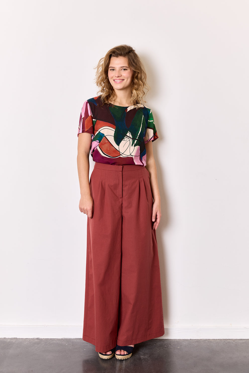 Woman wearing the Blake Trousers sewing pattern from Atelier Jupe on The Fold Line. A pants pattern made in cotton, linen, tencel, denim, fine wool, or corduroy fabric, featuring a mid-rise waist, double pleats at the front, darts at the back, side pockets, front zipper, and wide legs.