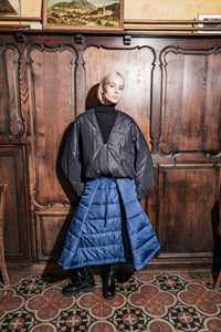 Woman wearing the Boaz Skirt sewing pattern from Fibre Mood on The Fold Line. A skirt pattern made in quilted fabric, water-repellent fabric, sturdy cotton, wool, or viscose fabric, featuring an elasticated waist with a drawstring, deep pleats, pockets, and midi length.