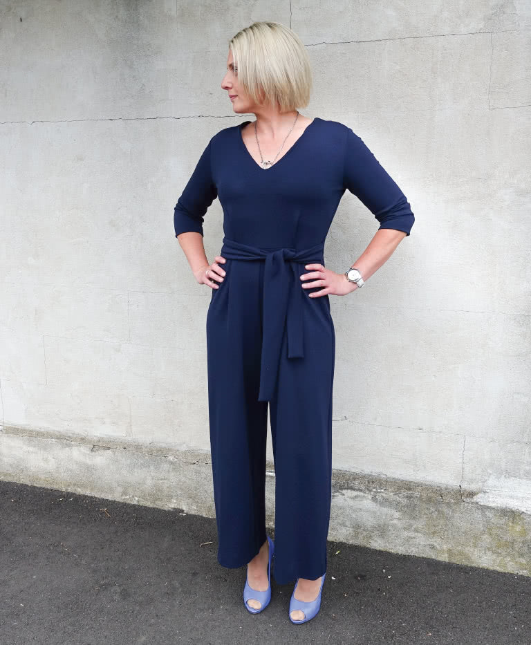 Woman wearing the Brice Knit Jumpsuit sewing pattern from Style Arc on The Fold Line. A jumpsuit pattern made in light ponte, sweater knit, jersey, or stretch silk fabric, featuring a V-neck, 3/4 length sleeves, tie belt, and ankle length.