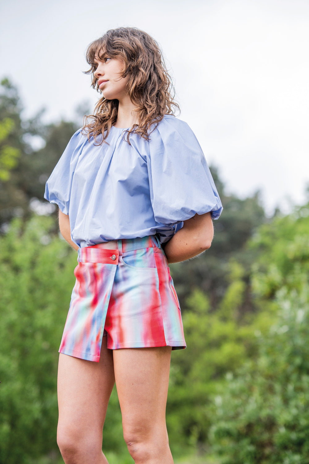 Woman wearing the Bruna Skort sewing pattern from Fibre Mood on The Fold Line. A skort pattern made in denim, cotton twill, fine corduroy, canvas, polycotton, woven jacquard, imitation leather, or nylon fabric, featuring an asymmetric crossover front, button closure, pockets, jeans styling, and mini length.