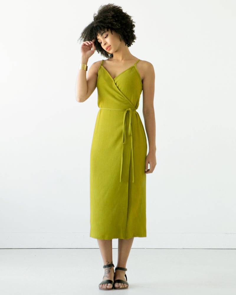 Woman wearing the Calvin Wrap Dress sewing pattern from True Bias on The Fold Line. A sleeveless dress pattern made in linen, chambray, rayon challis, silk crepe de chine, or cotton fabric, featuring a V-neck, adjustable shoulder straps, long waist ties, and midi length.