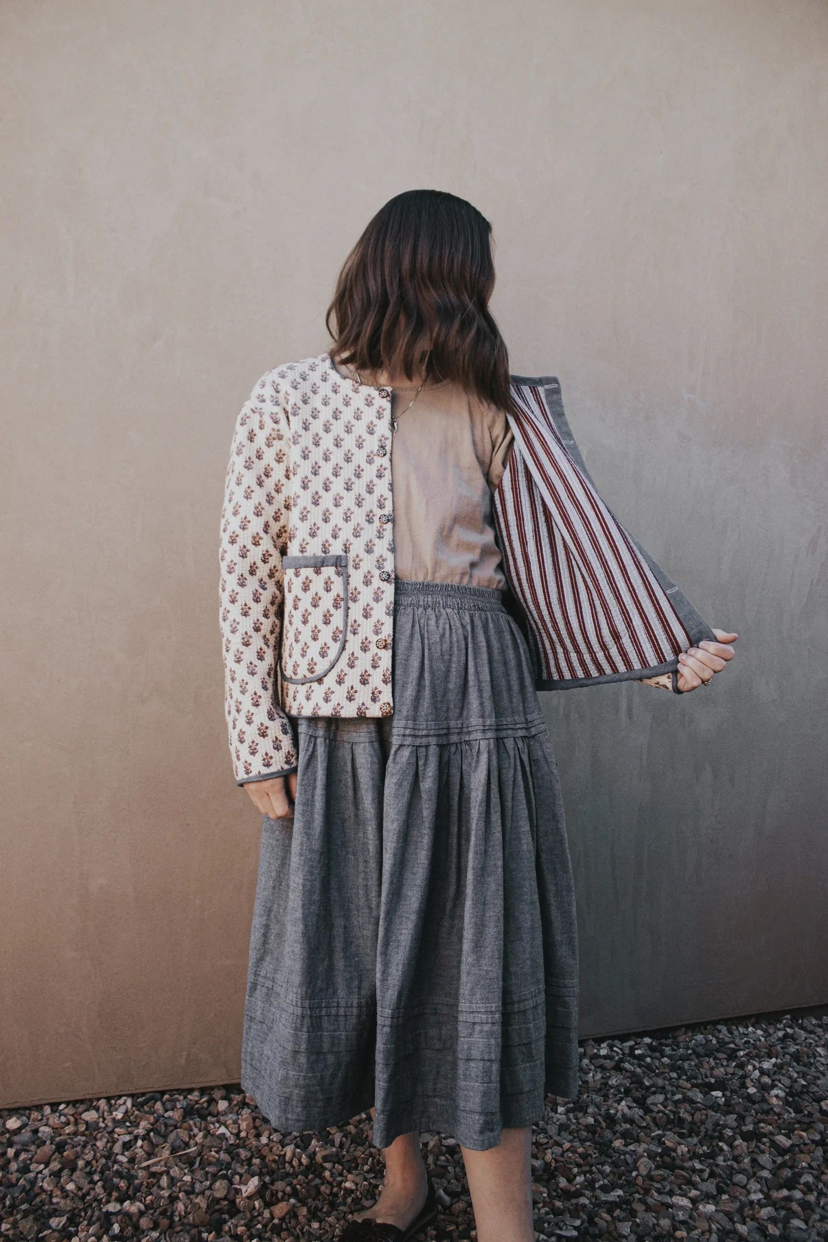 Woman wearing the Capella Coat sewing pattern from Madswick on The Fold Line. A quilted jacket pattern made in cotton, linen, or pre-quilted fabric, featuring a boxy fit, slight drop shoulder, button front, elasticated back hem, patch pockets, bias-bound seams, and reversible design.