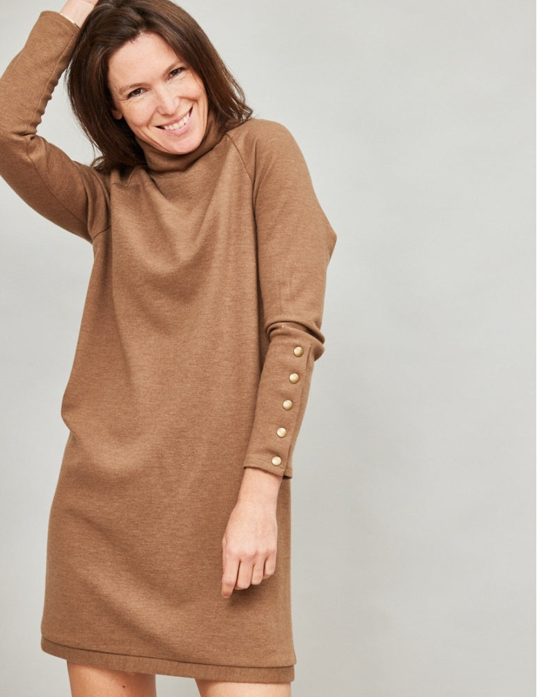 Woman wearing the Capsule Dress sewing pattern from Atelier Scämmit on The Fold Line. A sweater dress pattern made in knit fabric, featuring a turtleneck, raglan sleeves, long cuffs with snaps, and a mini length.
