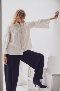 Woman wearing the Caren Blouse sewing pattern from Fibre Mood on The Fold Line. A shirt pattern made in muslin, chiffon, voile, or batiste fabric, featuring a pointed collar, yoke, gathering, a concealed button placket, and long sleeves with slits.