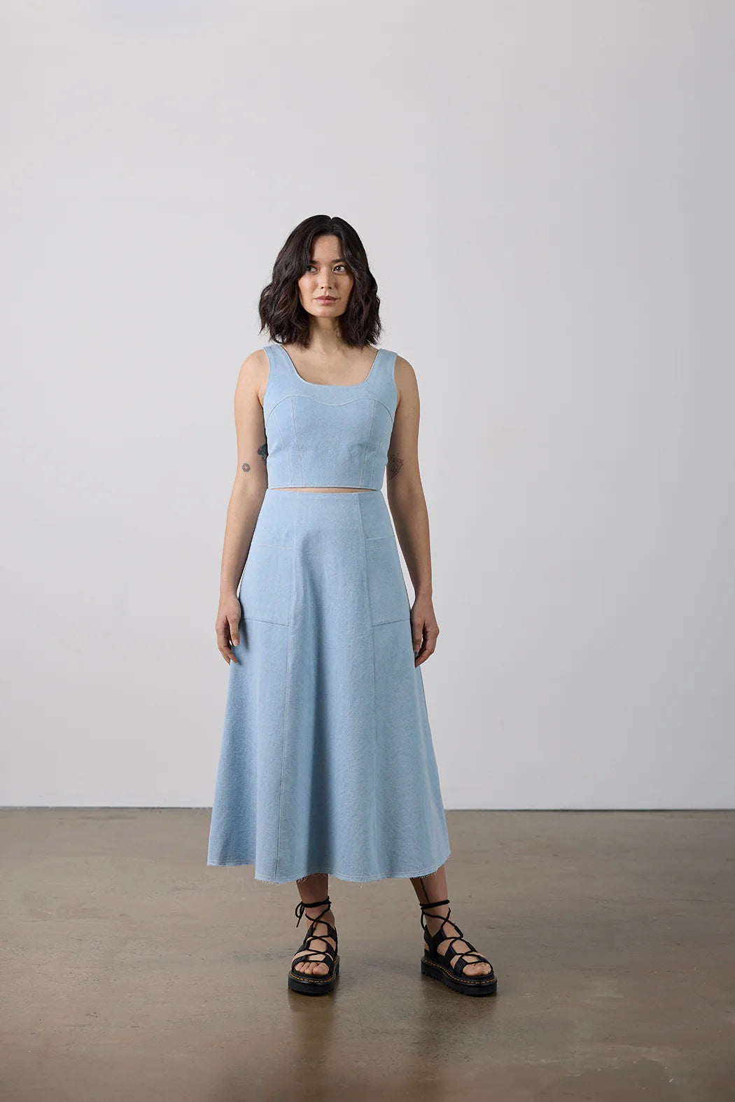 Woman wearing the Carey Top and Skirt sewing pattern from Elbe Textiles on The Fold Line. A top and skirt pattern made in denim, canvas, heavy weight linen, or structured cotton fabric, featuring a fitted sleeveless top with curved panels and a panelled A-line midi skirt with pockets.