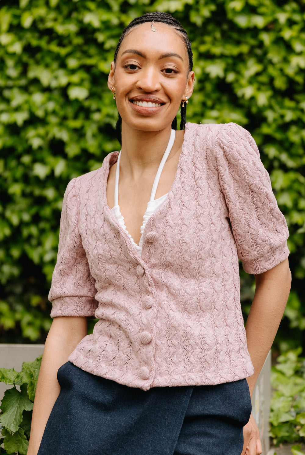 Woman wearing the Carlotta Cardigan sewing pattern from JULIANA MARTEJEVS on The Fold Line. A cardigan pattern made in knit fabric, featuring a V-neck, short puffed sleeves, and covered buttons.