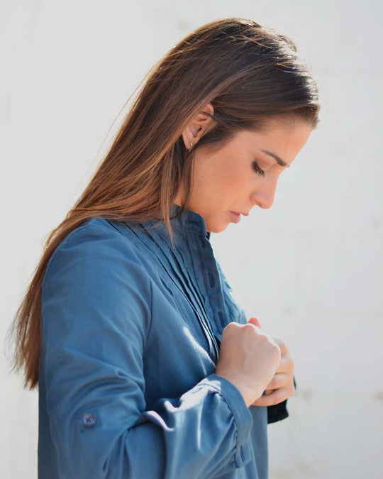 Woman wearing the Carme Blouse sewing pattern from Pauline Alice on The Fold Line. A shirt pattern made in cotton poplin, batiste, linen, chambray, or flannel fabric, featuring a band collar, pleated front yoke, popover button placket, and long sleeves with cuffs and button tabs to roll them up.