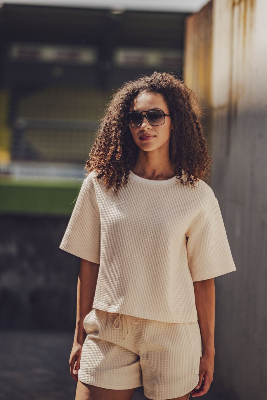 Woman wearing the Carmel Shorts sewing pattern from Fibre Mood on The Fold Line. A shorts pattern made in sweater fabric, French terry, structured jersey, or waffle fabric, featuring an elastic and drawstring waist, pockets, and inserts at the sides. 