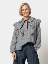Woman wearing the Cendrine Woven Blouse Set sewing pattern from Style Arc on The Fold Line. A top pattern made in seersucker, chambray, cotton lawn, crepe, or georgette fabric, featuring a ruffled round neckline with a front split and tie, bodice and shoulder frills, and long sleeves.