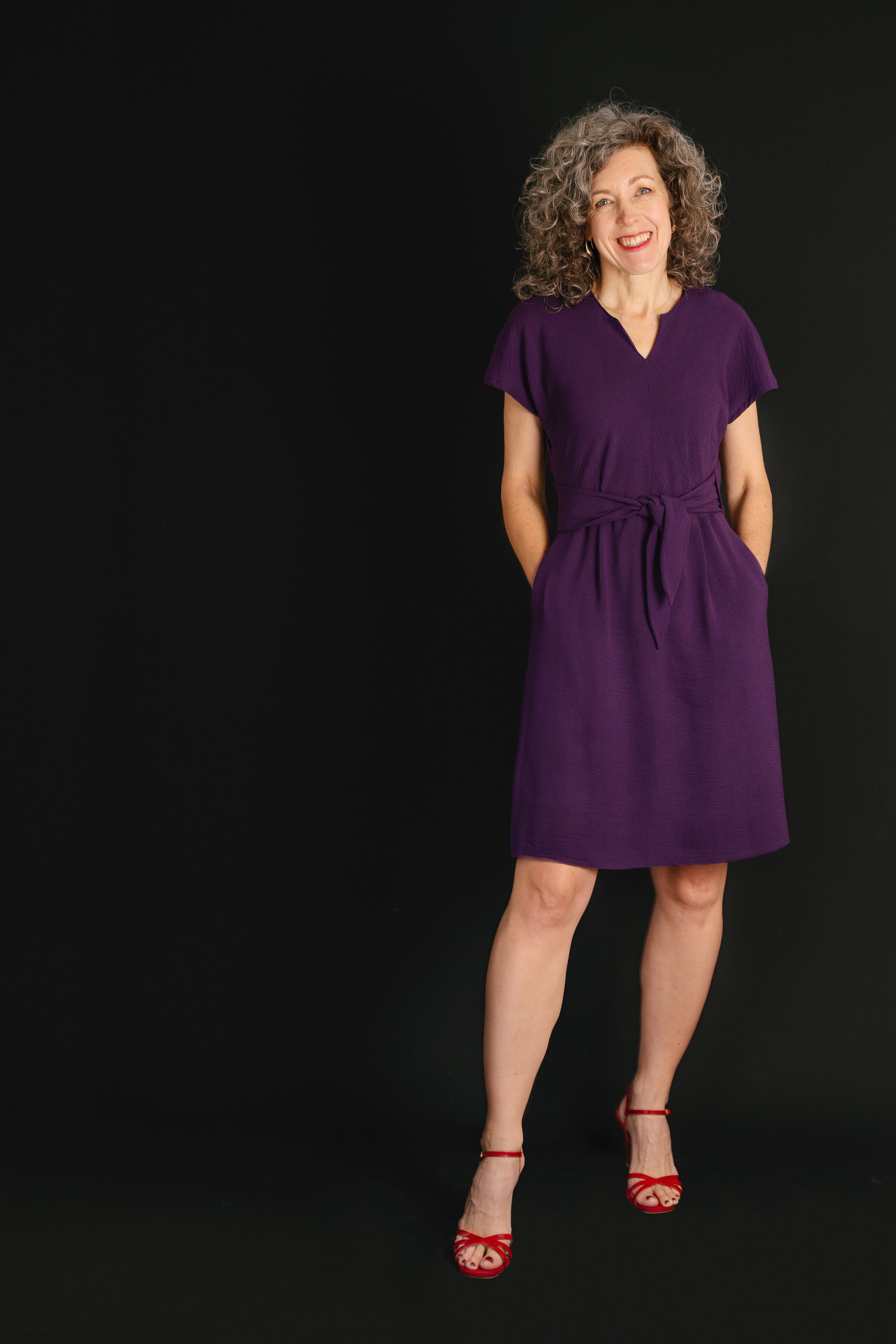 Woman wearing the Chacarita Wrap Dress sewing pattern from Liesl + Co on The Fold Line. A dress pattern made in linen, rayon, or soft cotton fabric, featuring a bias-cut top with a notch at the front neck, short sleeves, ties at the front waist, on-seam pockets, a V-neck at the back, and knee length.