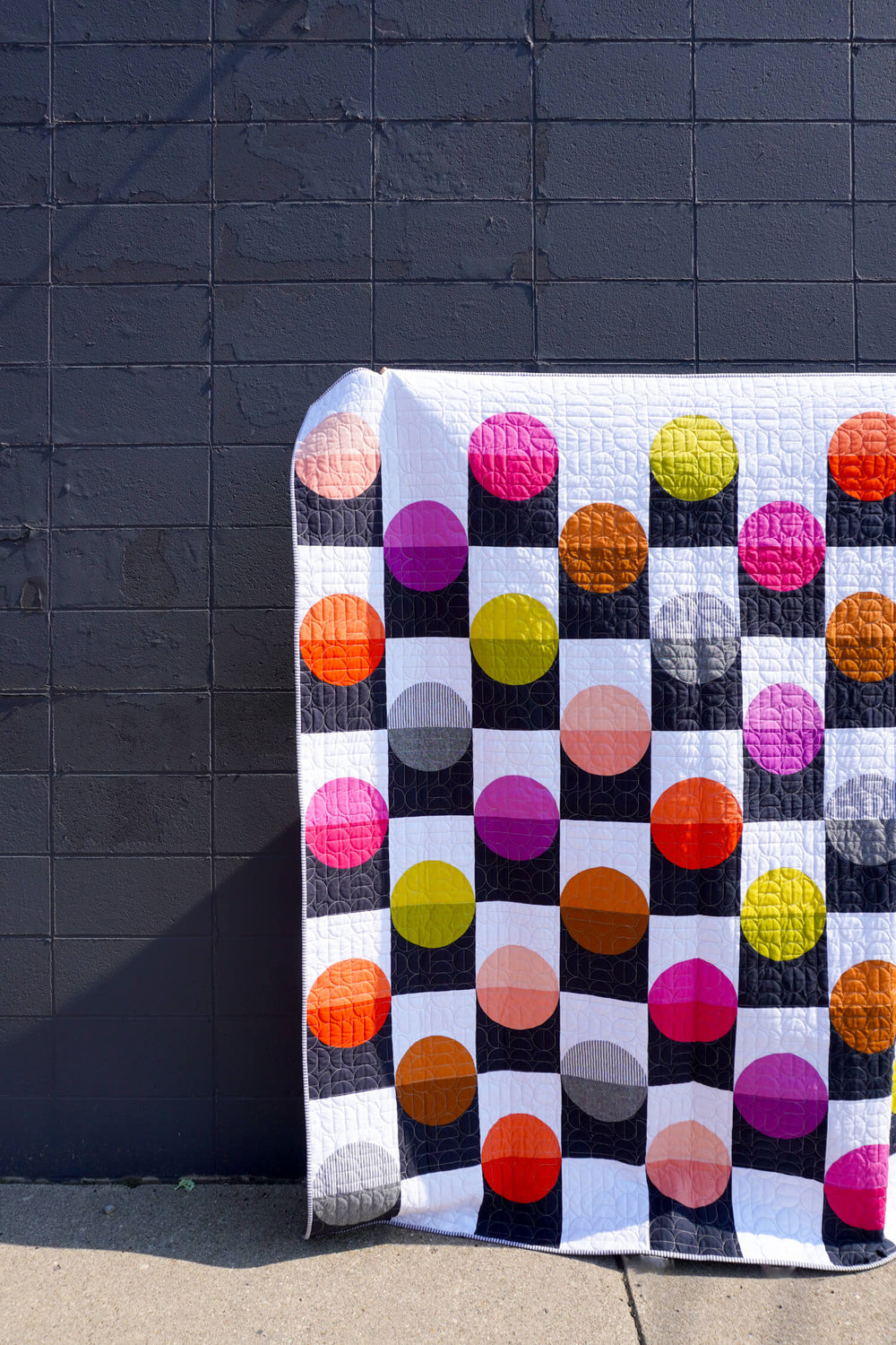 The Checkers Quilt sewing pattern from Modern Handcraft on The Fold Line. A quilt pattern made in quilting cotton fabric, featuring multicoloured circles on a black and white background.