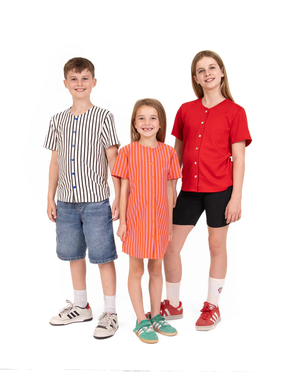 Children wearing the Child/Teen Ace Baseball Shirt sewing pattern from Little Rosy Cheeks on The Fold Line. A top pattern made in French terry/loopback sweatshirt, ponte roma, or cotton jersey fabric, featuring a drop shoulder, short sleeves, button or snap front, and gently curved hem.