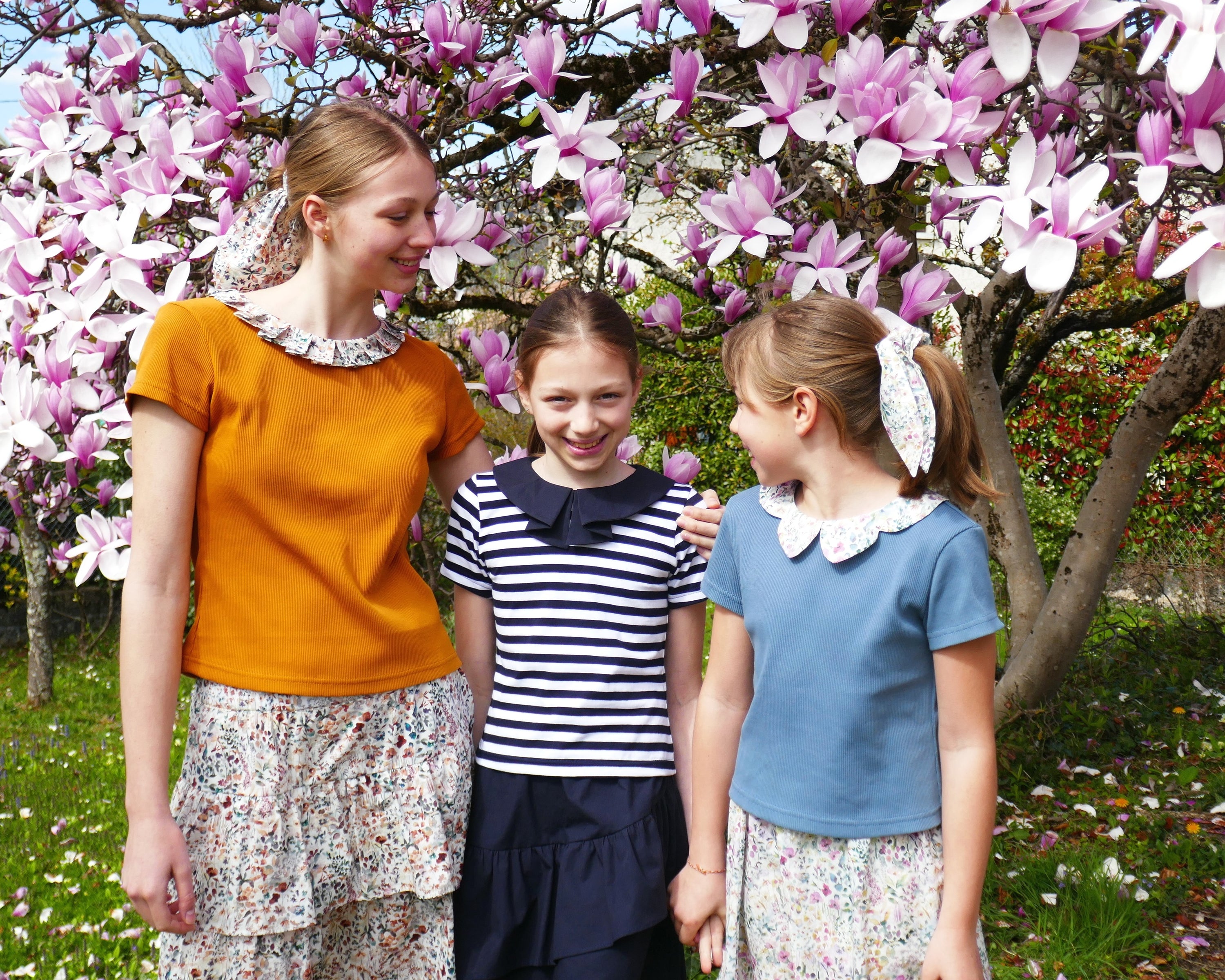 Girls wearing the Child/Teen Ende T-shirt sewing pattern from Petits D'om on The Fold Line. A T-shirt pattern made in knit fabric, featuring a slim fit, short sleeves, and a pleated or petal shaped woven collar.