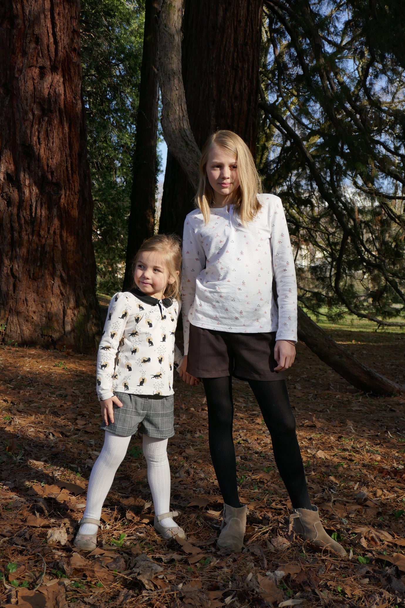 Girls wearing the Child/Teen Jeam Shorts sewing pattern from Petits D'om on The Fold Line. A shorts pattern made in cotton, poplin, denim, chambray, linen, thin wool, or velvet fabric, featuring an elasticated back waistband, box pleats, a zip fly, and back pockets with a folded detail.