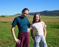 Girls wearing the Child/Teen Louve T-shirt sewing pattern from Petits D'om on The Fold Line. A tee pattern made in jersey fabric, featuring a round neckline, grown-on short sleeves, fitted waist, and optional pleats on one side.