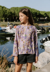 Girl wearing the Child/Teen Miss Violette Blouse sewing pattern from Maison Fauve on The Fold Line. A top pattern made in viscose rayon, lace, or silk fabric, featuring a round neckline, long sleeves, and a button placket and box pleat in back.