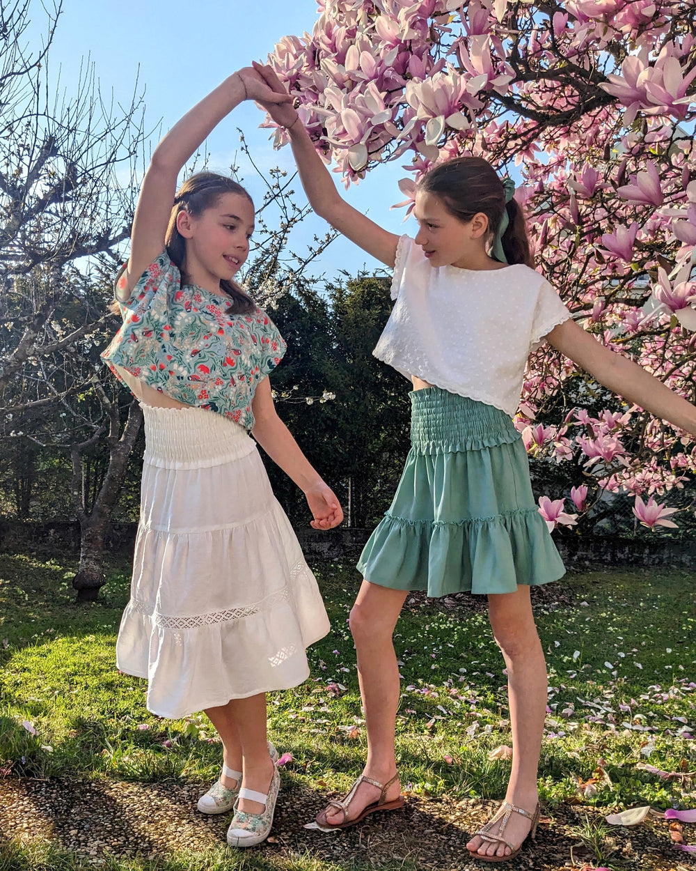 Girls wearing the Child/Teen Querida Skirt sewing pattern from Petits D'om on The Fold Line. A skirt pattern made in Liberty, light cotton, batiste, viscose, tencel, or crepe fabric, featuring a shirred waist and gathered tiers.