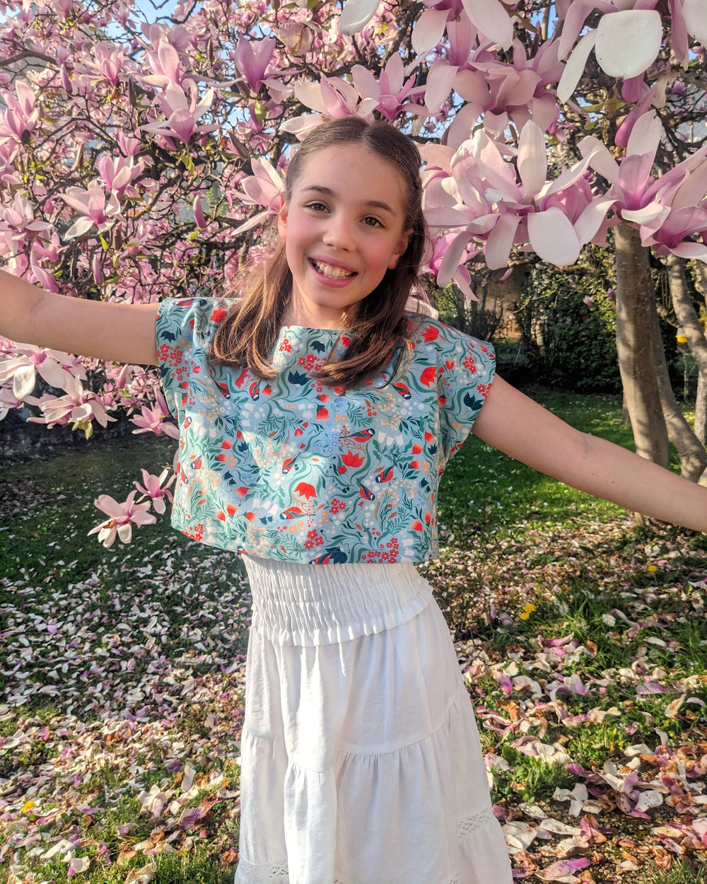 Girl wearing the Child/Teen Xeres Top sewing pattern from Petits D'om on The Fold Line. A lined top pattern made in Liberty print, lightweight cotton, broderie anglaise, batiste, viscose, or tencel fabric, featuring a cropped and oversized fit and grown-on short sleeves.