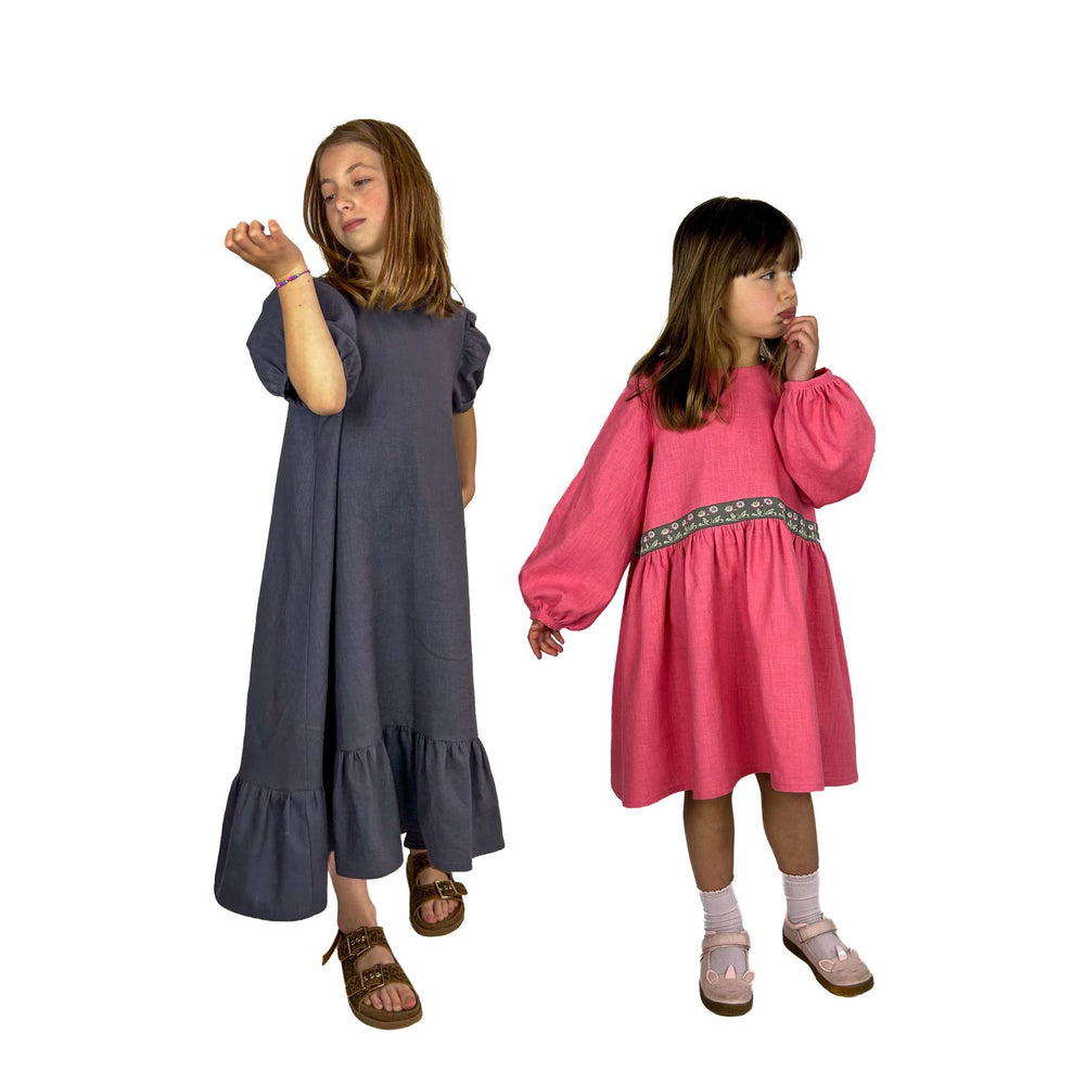Girls wearing the Children's May Dress sewing pattern from Dhurata Davies Patterns on The Fold Line. A dress pattern made in linen, cotton chambray, poplin, lawn, double gauze, or needle cord fabric, featuring an A-line silhouette, high-low hem, gathered skirt or ruffled hem, and short puff sleeves or long bishop sleeves.