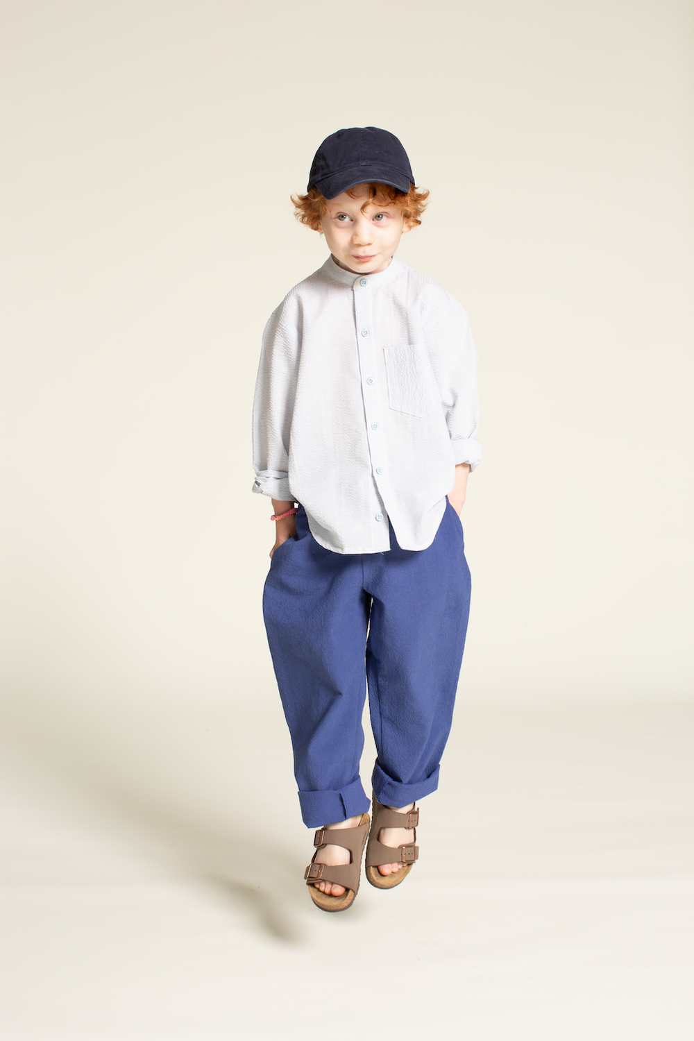 Boy wearing the Children's Mini Jensen Shirt sewing pattern from Wardrobe by Me on The Fold Line. A shirt pattern made in cotton oxford, poplin, denim, flannel, linen, or silk fabric, featuring a band collar, front button placket, long sleeves, chest pocket, and curved hem.