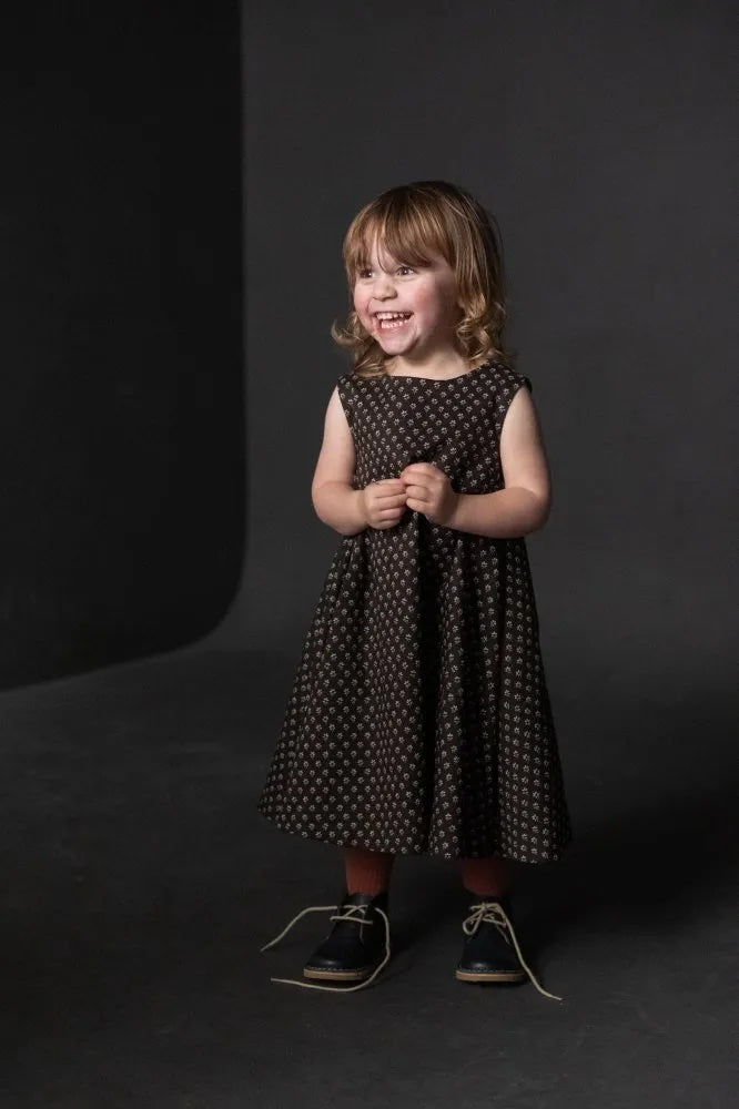 Girl wearing the Children's Trapezette Dress sewing pattern from Merchant & Mills on The Fold Line. A sleeveless dress pattern made in linen, Indian handlooms, blockprints, soft denim chambray, fine corduroy, soft wool or tweed fabric, featuring a trapeze shape and button and loop back neck closure.