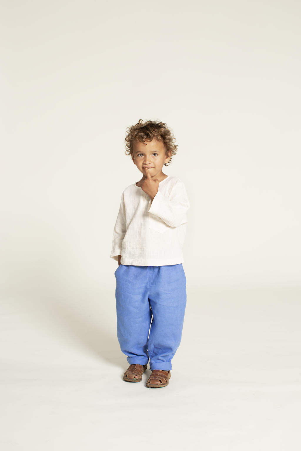 Boy wearing the Children's Volume Pants sewing pattern from Wardrobe by Me on The Fold Line. A pants pattern made in cotton oxford, poplin, denim, flannel, linen, or silk fabric, featuring a roomy fit, elastic waist, side seam pockets, and back pockets.