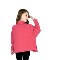 Girl wearing the Children's Wren Pullover sewing pattern from Dhurata Davies Patterns on The Fold Line. A top pattern made in french terry, fleece or loop backed sweatshirt fabric, ponte roma, or double knit jersey fabric, featuring a high neck, long raglan sleeves, side vents with mitred corners, and a high-low hem. 