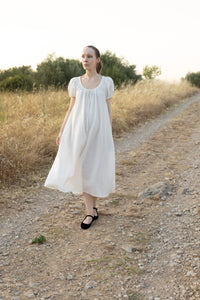 Woman wearing the Chloe Dress sewing pattern from Silversaga Patterns on The Fold Line. A vintage-inspired dress pattern made in cotton or linen fabric, featuring an adjustable scoop neckline with fabric ties, short puff sleeves, hidden in-seam pockets, and midi length.