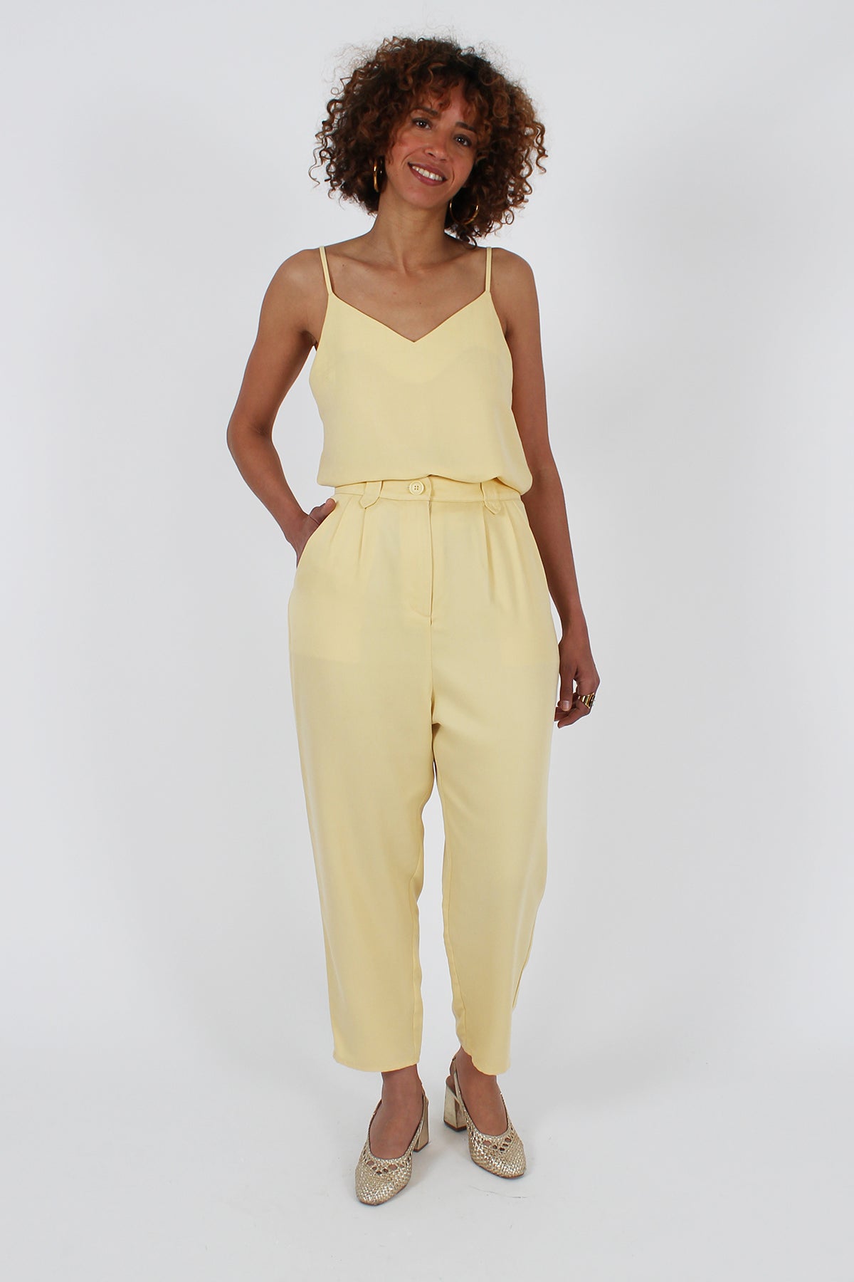 Woman wearing the Christophine Trousers sewing pattern from I AM Patterns on The Fold Line. A trousers pattern made in crepe, tencel twill, viscose twill, silk, lightweight denim, or linen fabric, featuring a classic jodhpur shape with a slightly dropped crotch and generous ease around the hips, front pleats, zip fly, pointy belt loops, slanted side pockets, back patch pockets, and a tightening tab at the back.