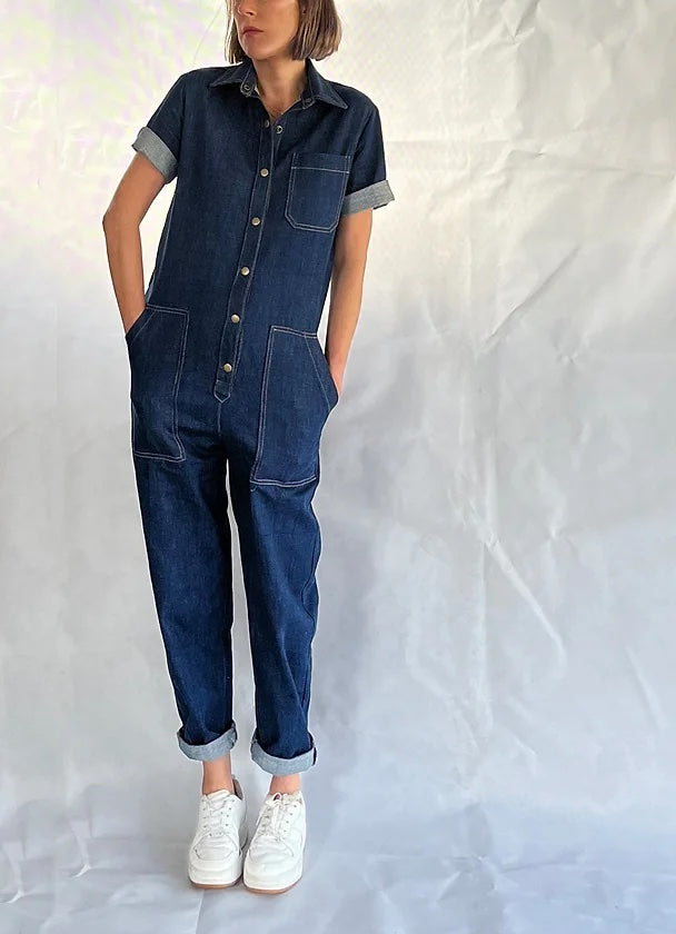 Woman wearing the Circa Overalls sewing pattern from French Navy on The Fold Line. A boiler suit pattern made in linen, denim, cotton twill, or corduroy fabric, featuring a relaxed fit, snap button placket, short sleeves, utility pockets, partially elasticated waist, and tapered legs.