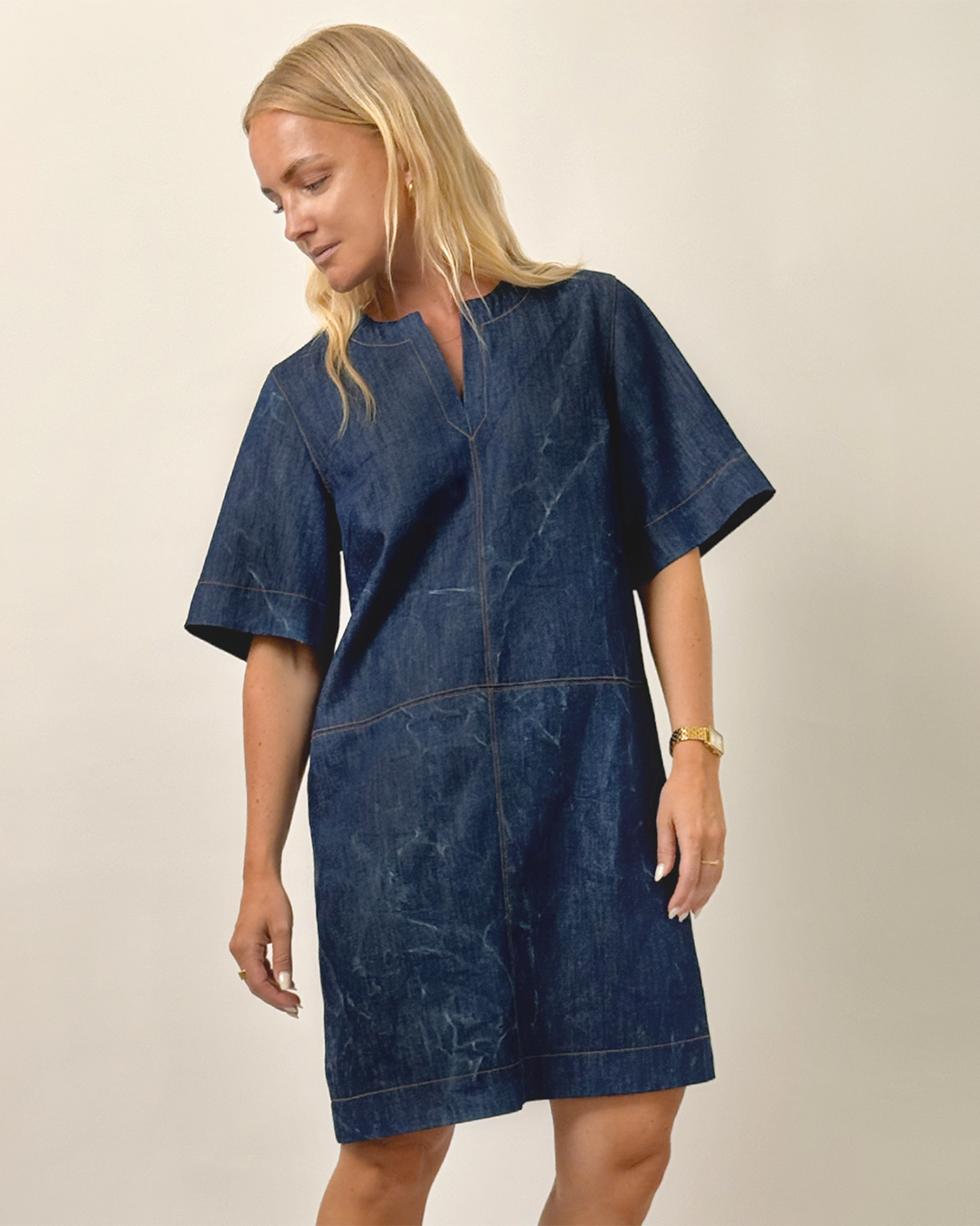 Woman wearing the City Dress sewing pattern from Wardrobe by Me on The Fold Line. A dress pattern made in denim, cotton twill, linen, chambray, or viscose-linen blend fabric, featuring a slightly A-line shape, notched neckline, wide elbow length sleeves, decorative seamlines, and above-the-knee length. 