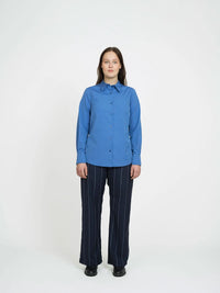 Woman wearing the Classic Shirt sewing pattern from The Assembly Line on The Fold Line. A shirt pattern made in light to medium weight fabric, featuring a collar and stand, folded button placket, bust darts, back darts, long sleeves with cuffs, and a rounded hem.